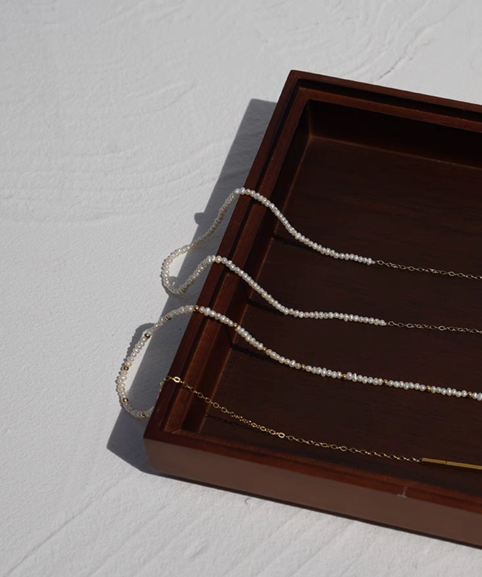 Rice pearl necklace with 14K gold-filled accents showing Style A and Style B together on wooden tray with delicate freshwater pearls and gold chain