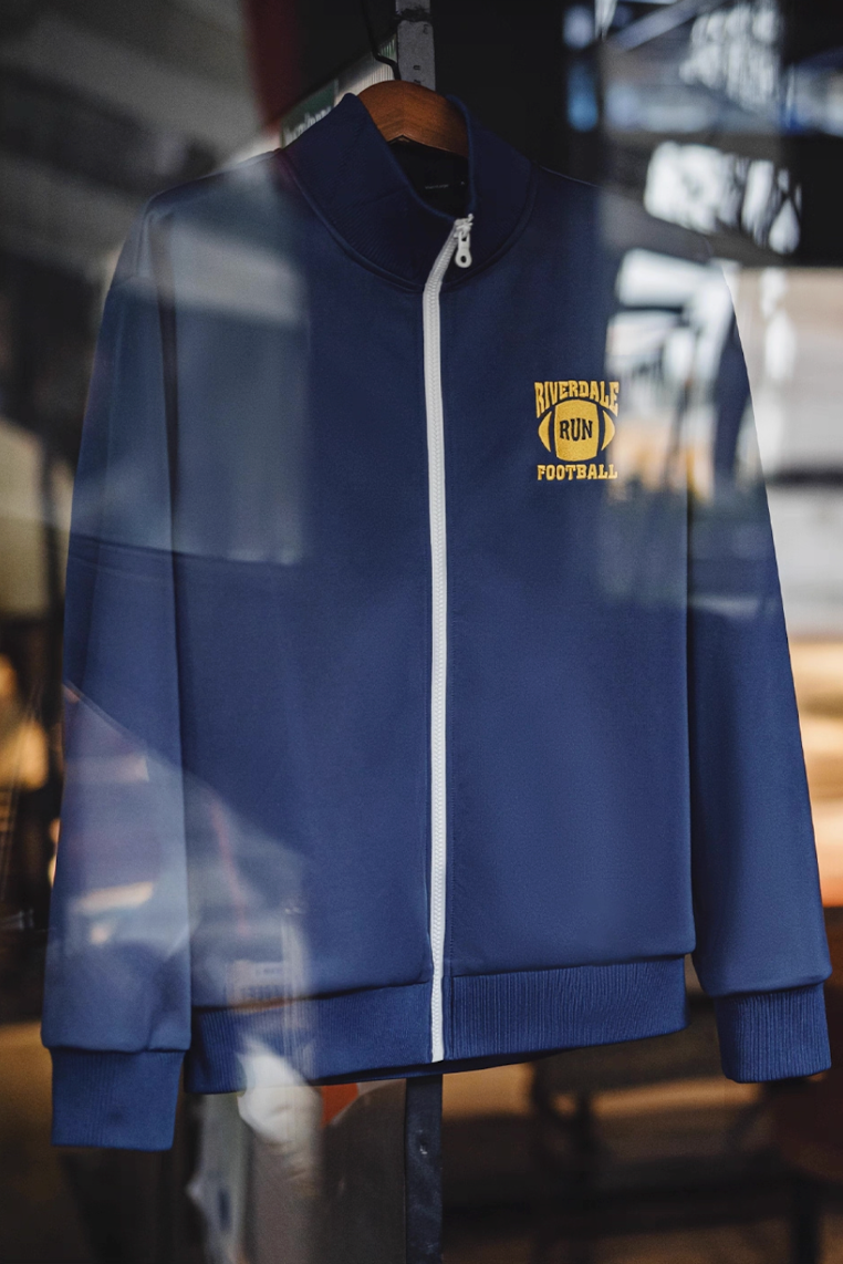 Riverdale Run navy track jacket on hanger showing yellow football logo