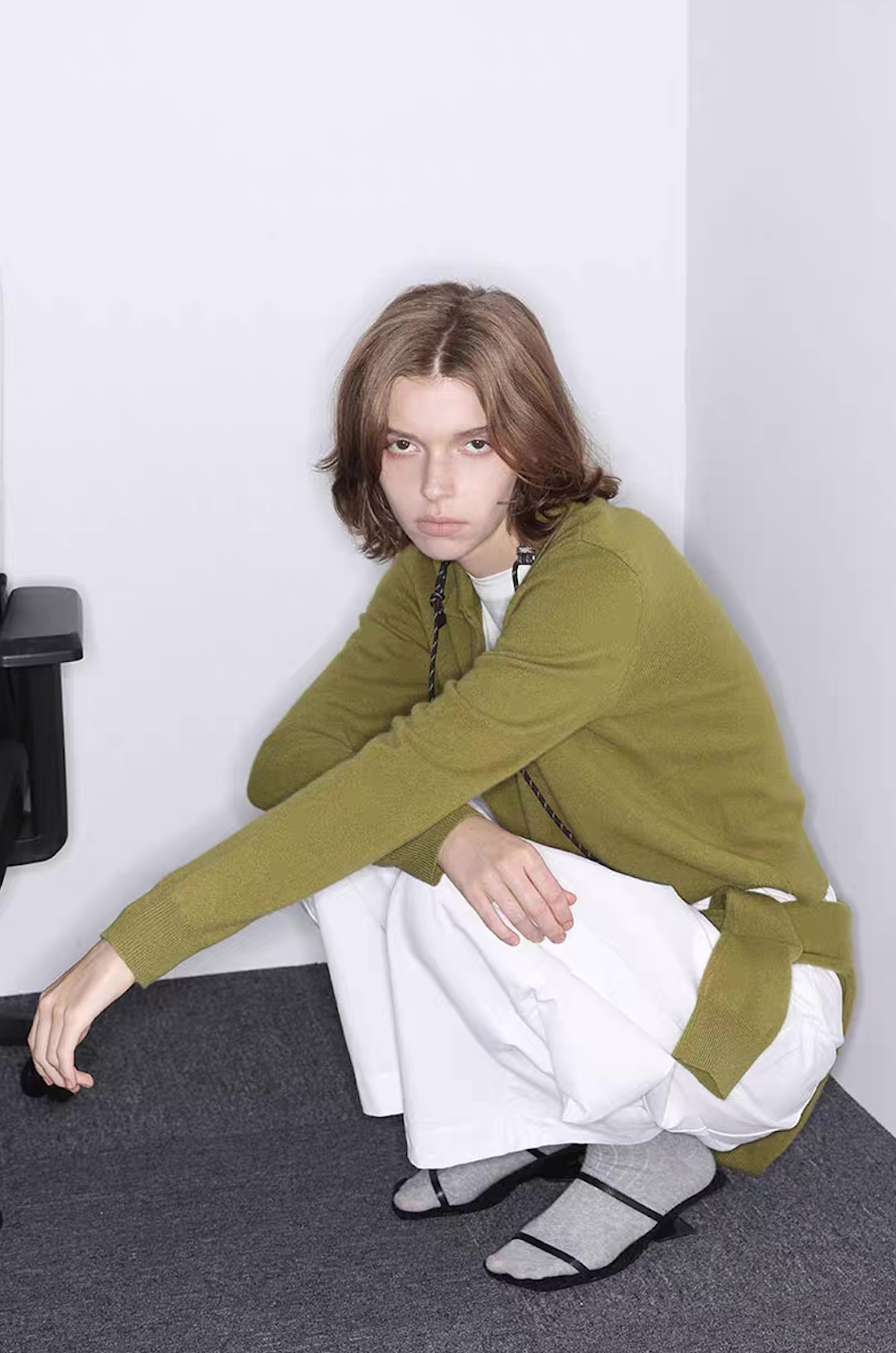 Model wearing green cashmere wool polo sweater with white wide pants, seated pose