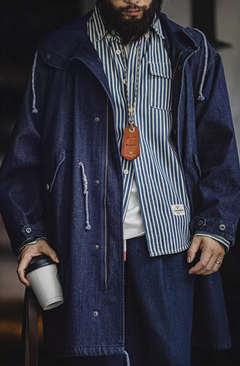 Model wearing M-51 denim fishtail parka over striped shirt holding coffee