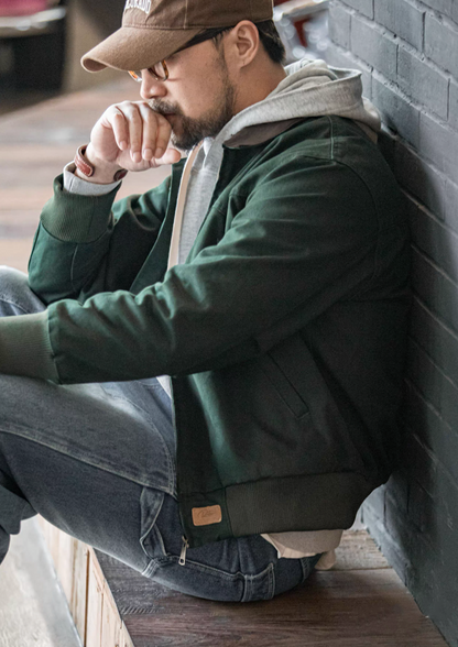 Model sitting by wall wearing dark green Santafe workwear jacket with corduroy collar.