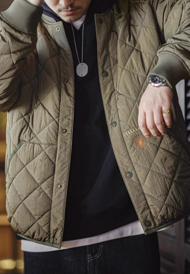 Man layering army green quilted bomber jacket over black hoodie