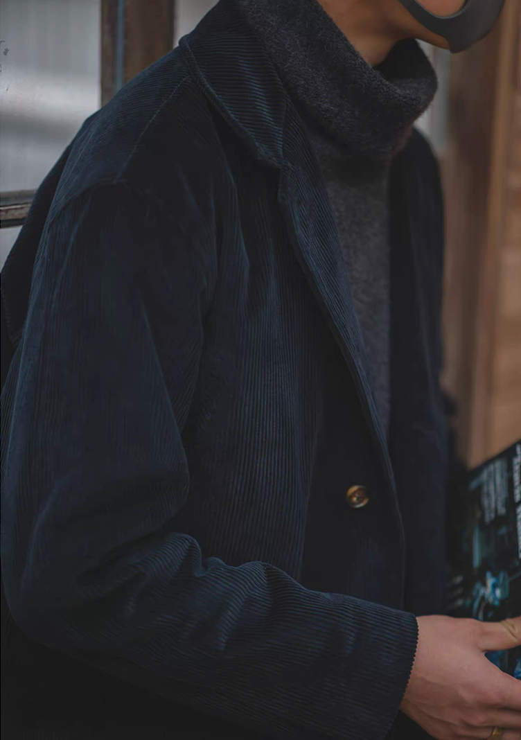 Side profile of men’s navy corduroy long coat styled with grey turtleneck.