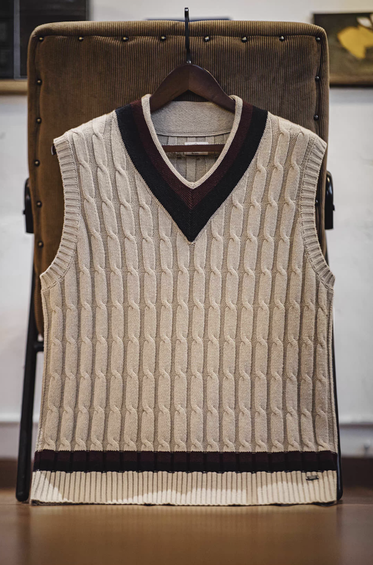 Ivy-style khaki sweater vest hanging on chair showcasing cable knit pattern