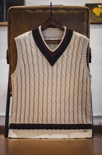 Ivy-style khaki sweater vest hanging on chair showcasing cable knit pattern