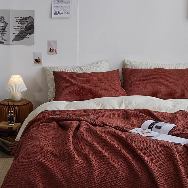 Burgundy 3D honeycomb waffle cotton throw blanket placed over white bedding with matching pillow covers in a warm bedroom scene.