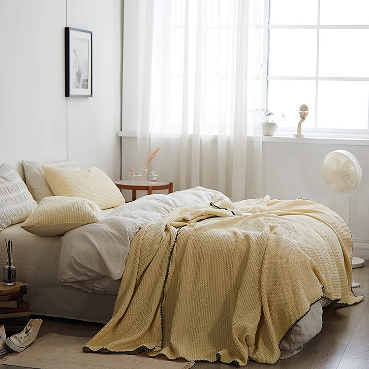 Light yellow waffle honeycomb cotton throw blanket layered over white bedding in a bright modern bedroom with natural sunlight.