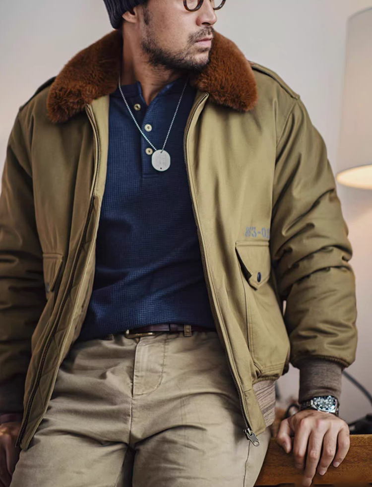 Model seated indoors wearing B-10 jacket over navy waffle-knit shirt and khaki pants.