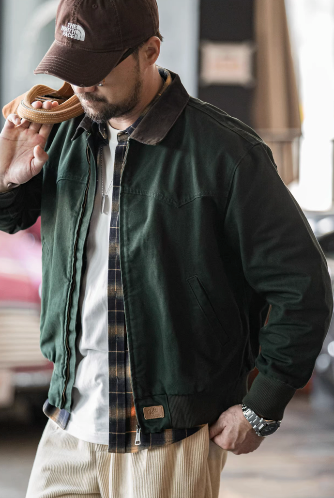 Man in dark green canvas workwear bomber jacket styled with plaid shirt underneath.