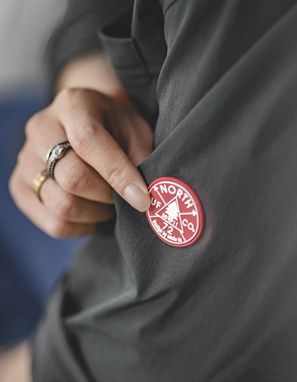 Close-up of red North utility badge on sleeve of dark charcoal overshirt jacket.