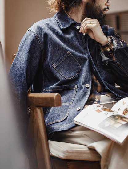 Man sitting in chair wearing 14 oz denim utility jacket reading a magazine