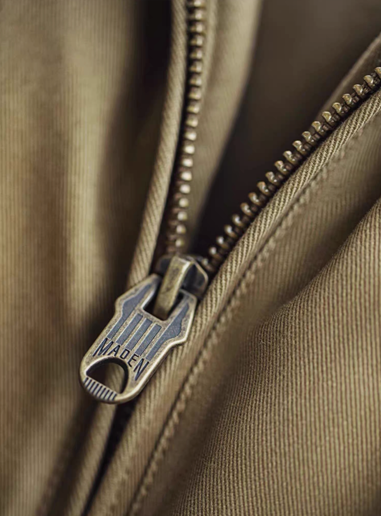 Macro close-up of metal zipper engraved “MADE IN,” showing durable cotton weave texture.