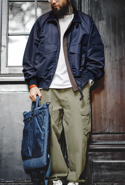 Full-body shot of model wearing G-8 Navy Flight Jacket holding a navy backpack in street setting.
