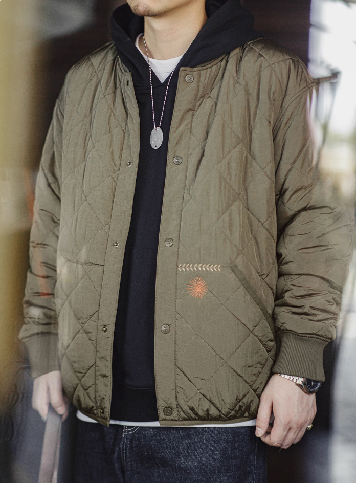 Model wearing olive quilted bomber jacket over layered streetwear look