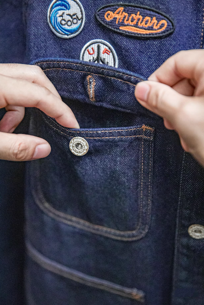Close-up of front pocket button detail on denim workwear coat