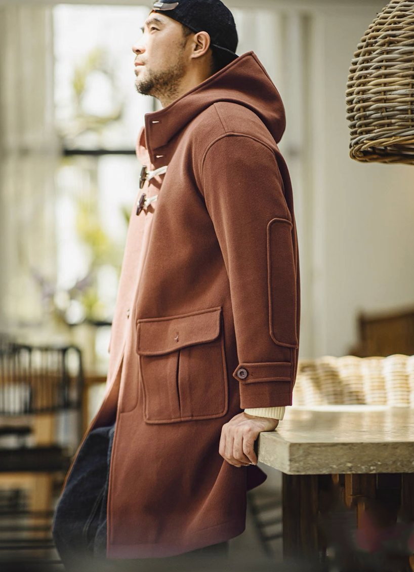 Man in brown toggle coat leaning casually by a table