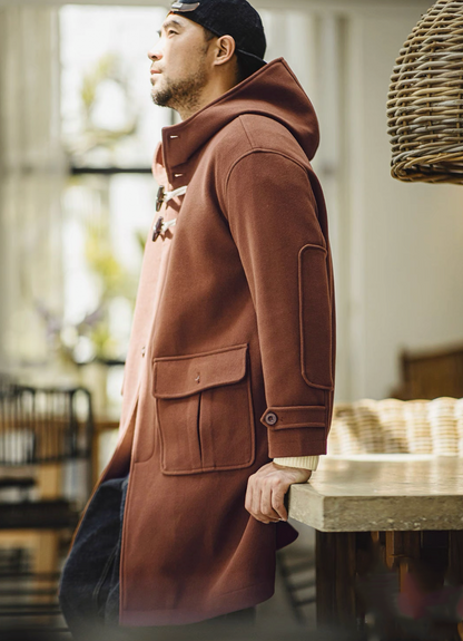 Man in brown toggle coat leaning casually by a table