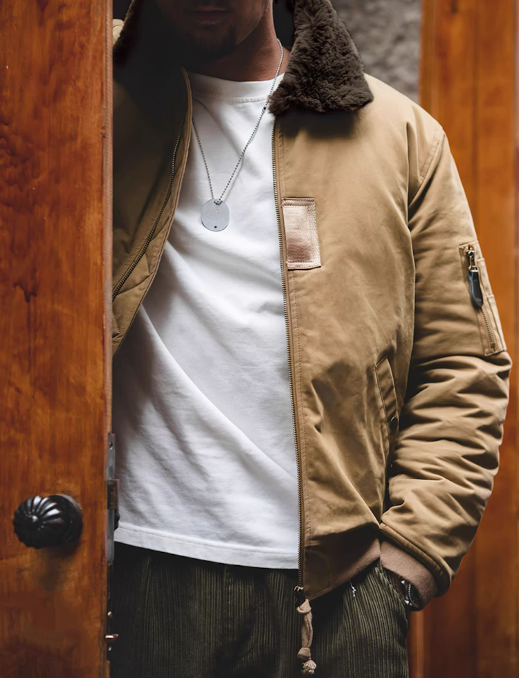 Man wearing khaki B-15 flight jacket standing by doorway