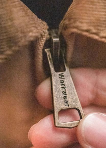 Close-up of brass zipper pull engraved with Workwear text on khaki Santafe jacket.