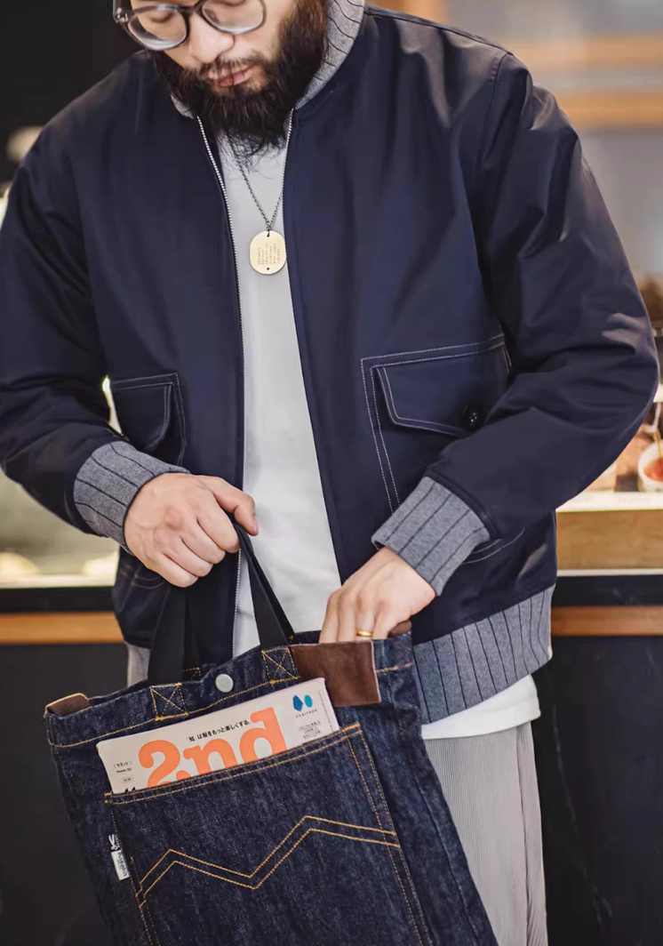 Man wearing navy bomber jacket holding denim tote bag