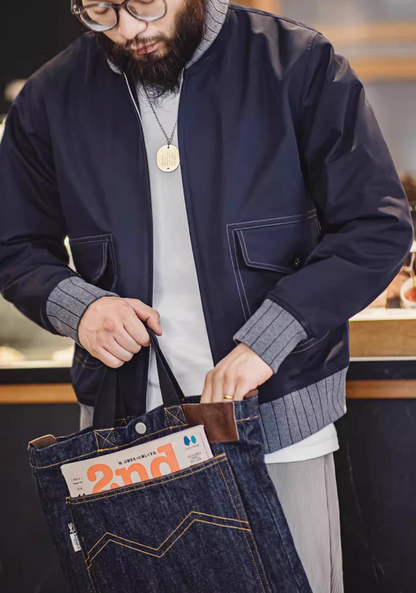 Man wearing navy bomber jacket holding denim tote bag