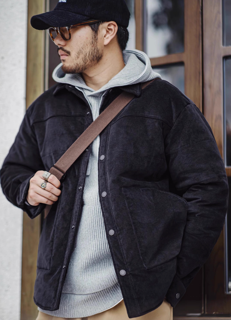 Man in navy blue corduroy jacket and hoodie standing by window