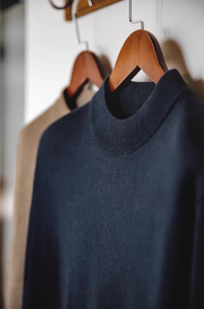 Navy blue sweater hanging on wooden hanger close-up neck detail