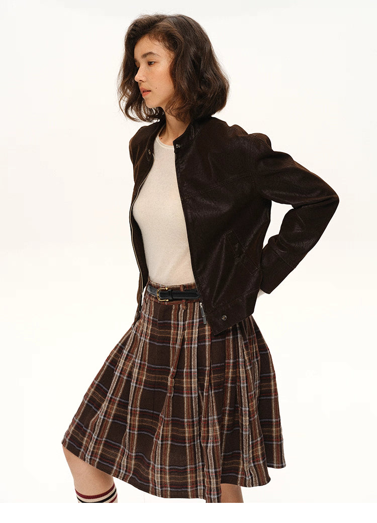 Woman styling cocoa moto jacket with plaid skirt, showing short structured silhouette.