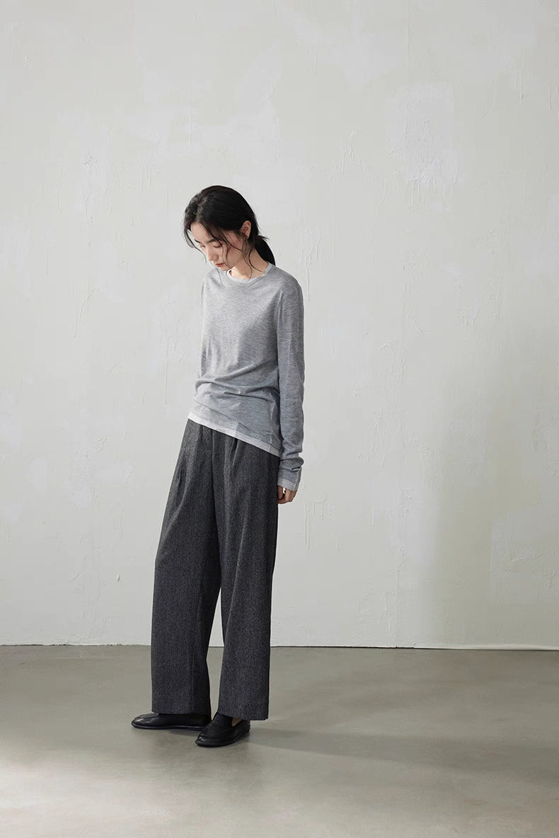 Model looking down wearing light gray layered knit top and gray pants softly lit