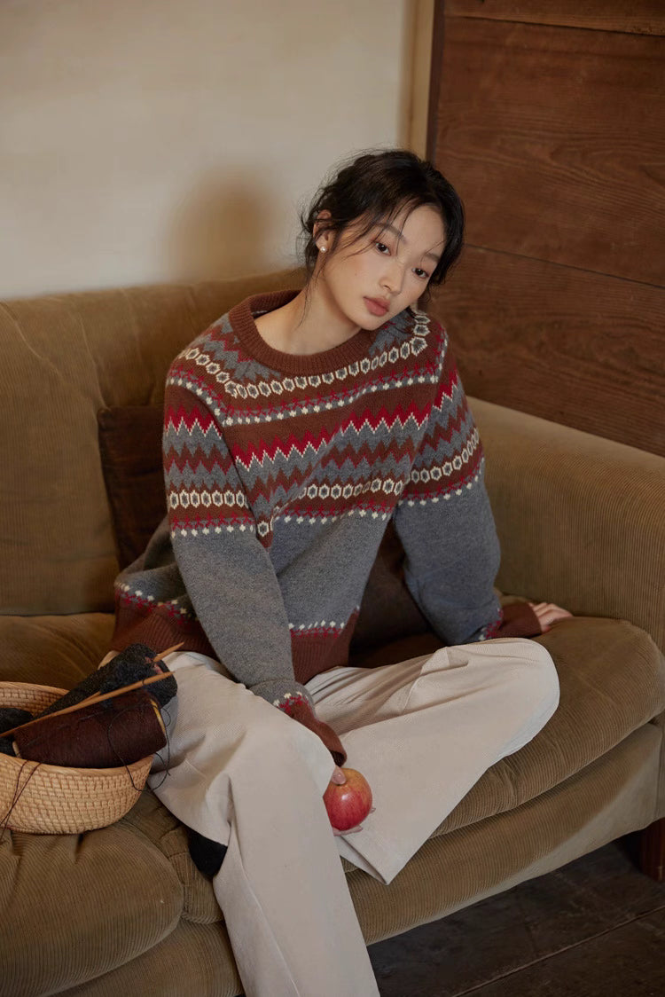 Relaxed portrait of model wearing gray-red patterned wool sweater sitting casually