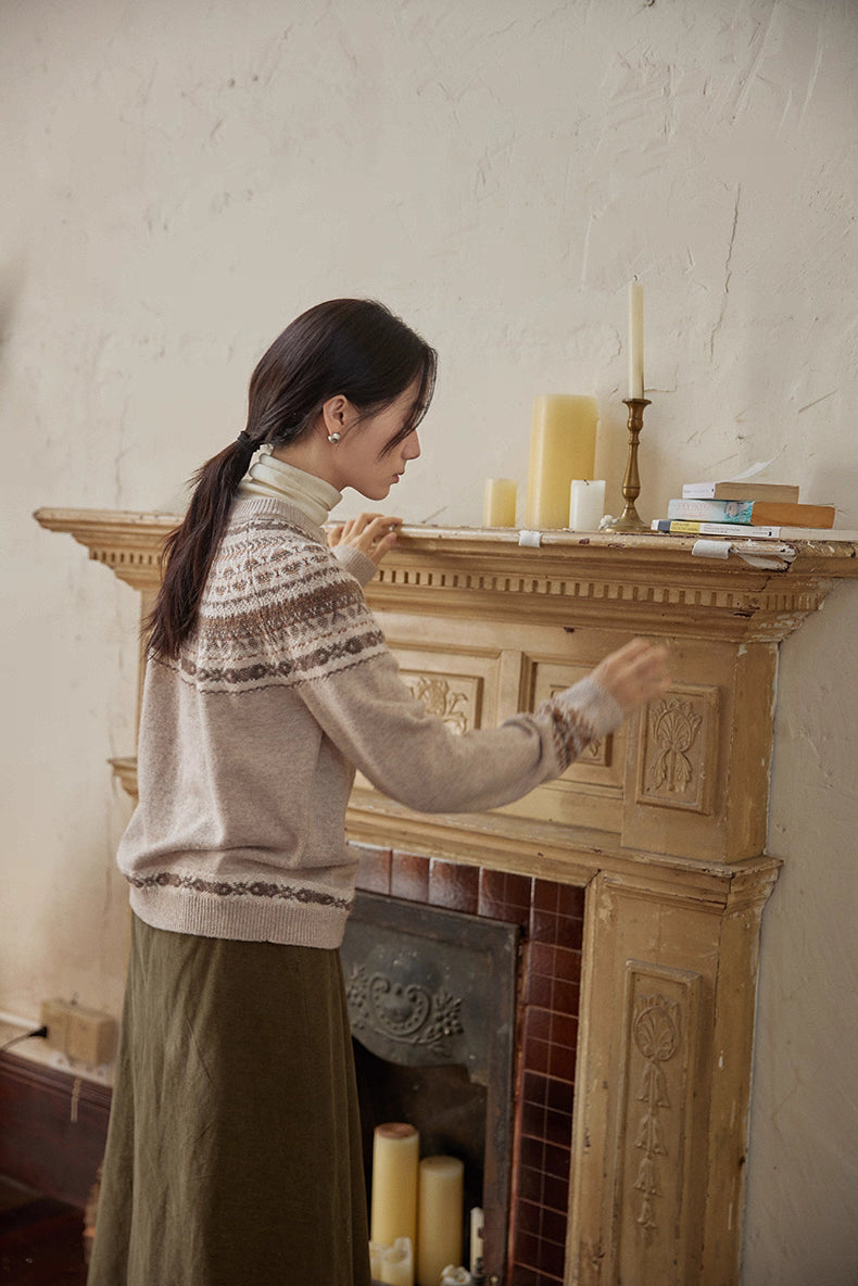 Side-back view of model adjusting candles on fireplace wearing beige Fair Isle cardigan