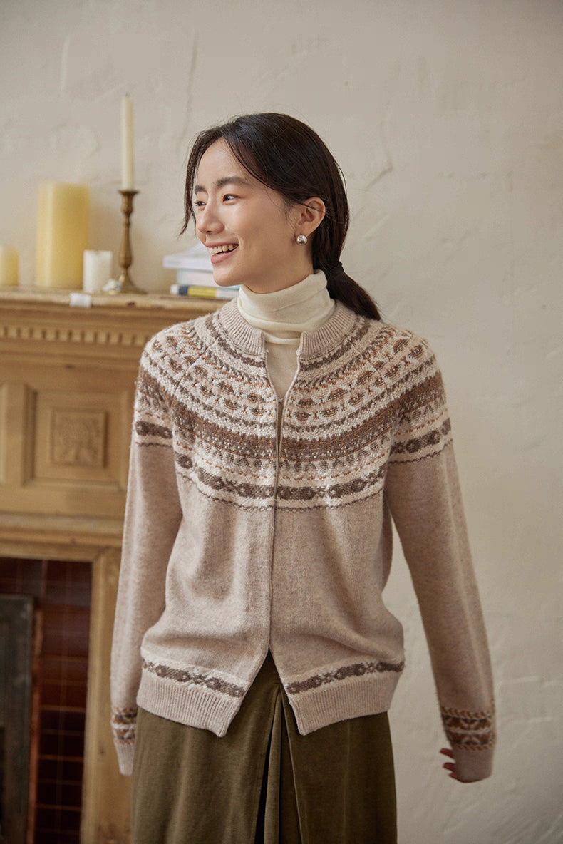 Model smiling in beige-brown Fair Isle cardigan layered over ivory turtleneck beside fireplace