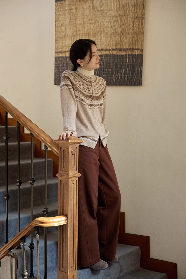 Model wearing beige Fair Isle cardigan and brown trousers leaning on staircase railing