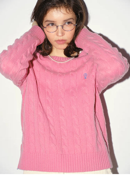 Woman wearing a rose pink pure wool cable-knit sweater with hands behind her neck, close-up front portrait, soft winter knit styling.