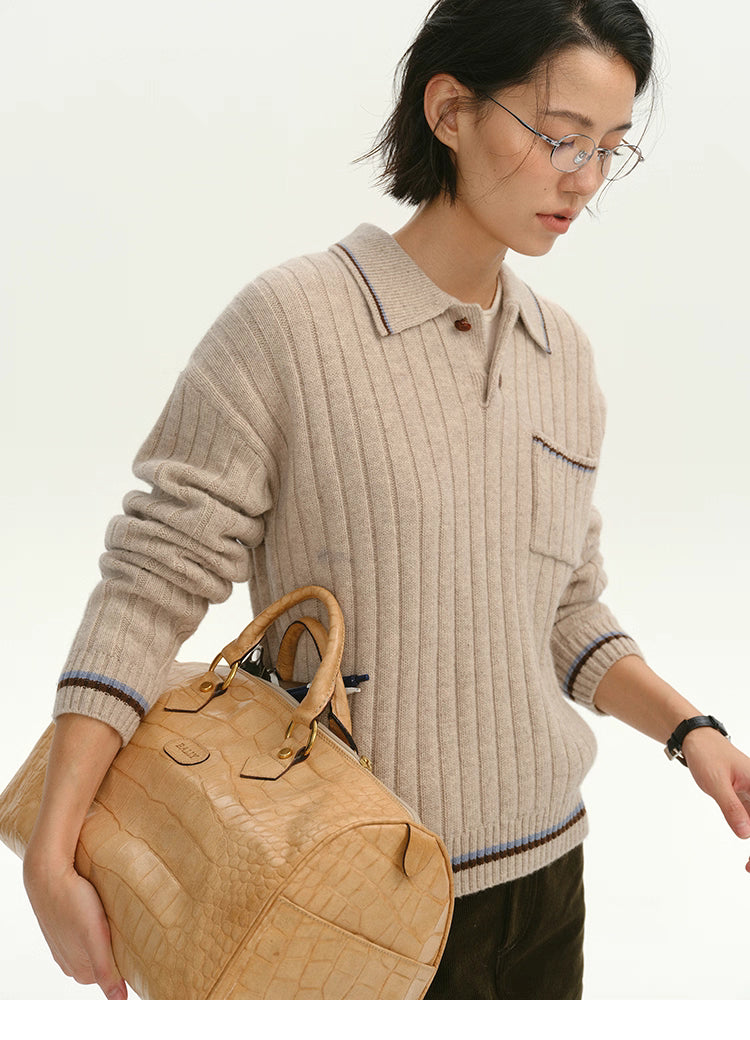 Side view of model carrying a tan bag while wearing the rib-knit wool polo sweater.
