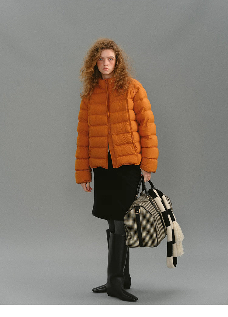 Full-body shot of model wearing a warm orange matte down puffer with skirt and boots.