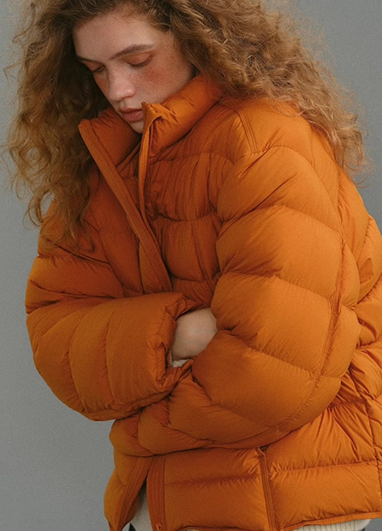 Side view of warm orange AirSoft down puffer as the model folds her arms.