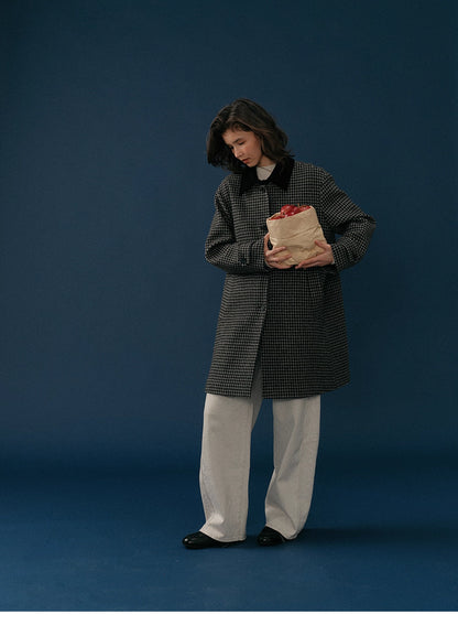 Model wearing a midnight houndstooth wool coat holding a paper bag of apples in a full-body shot.