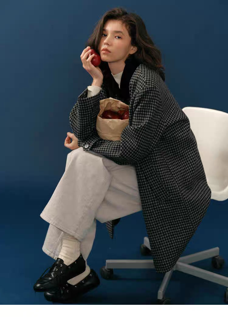 Seated model holding an apple while wearing a midnight houndstooth wool coat with soft collar.
