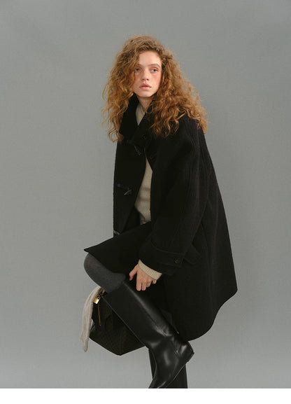 Model seated wearing black toggle coat and tall black boots.