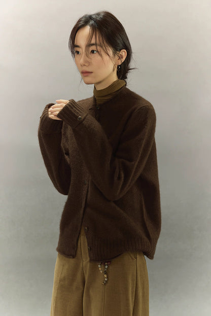 Woman wearing dark coffee brown yak wool round-neck cardigan with turtleneck base layer, standing with hands together