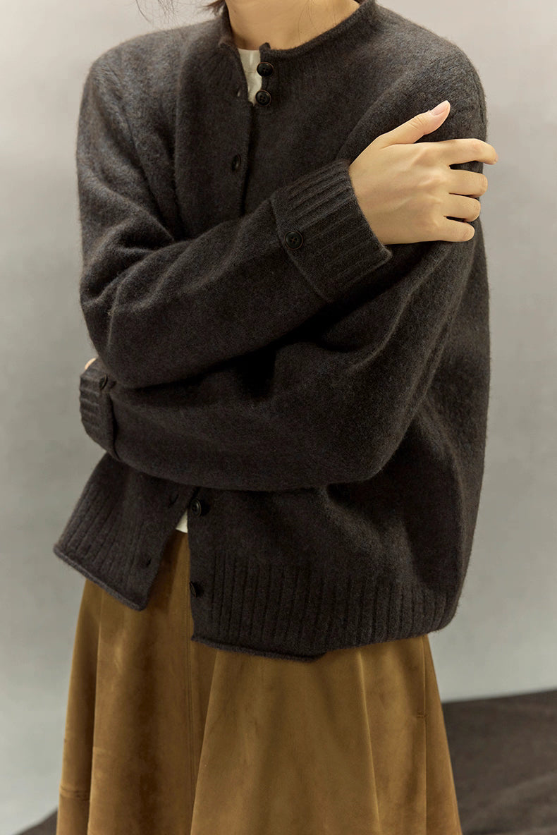 Charcoal gray yak wool round-neck cardigan shown from the front with arms crossed, rib hem and buttons visible