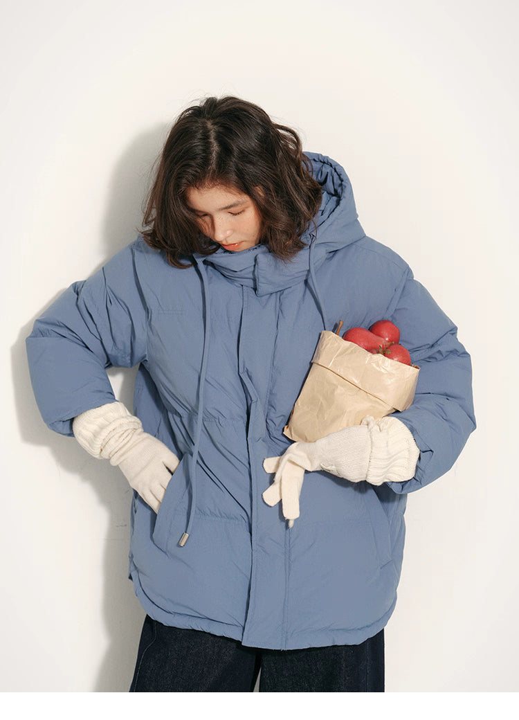 Dusty blue puffer jacket front view as the model looks down while holding apples in one hand.