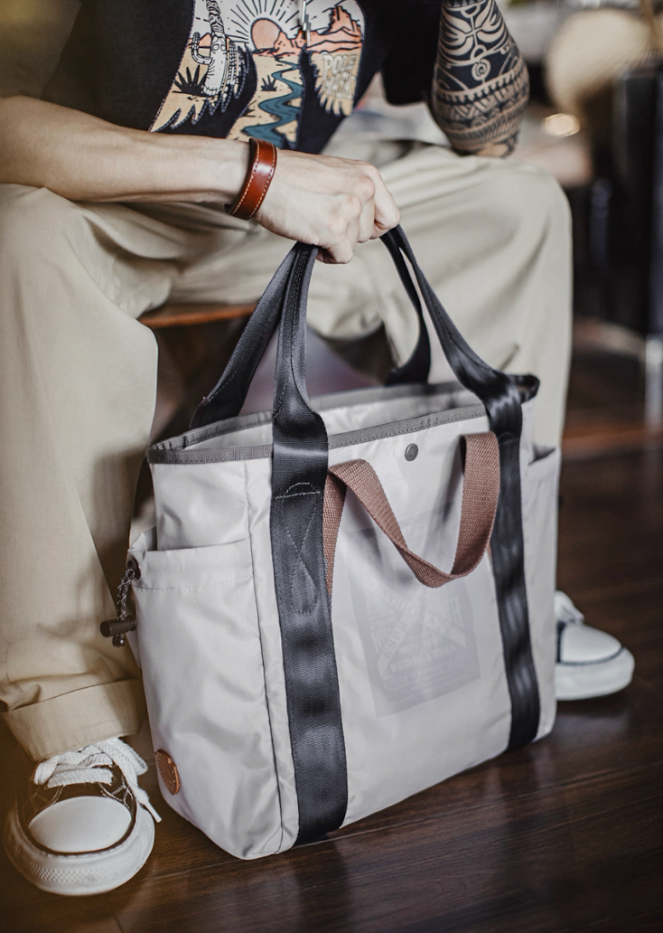 Model seated holding Ash Gray water-resistant tote bag with black straps