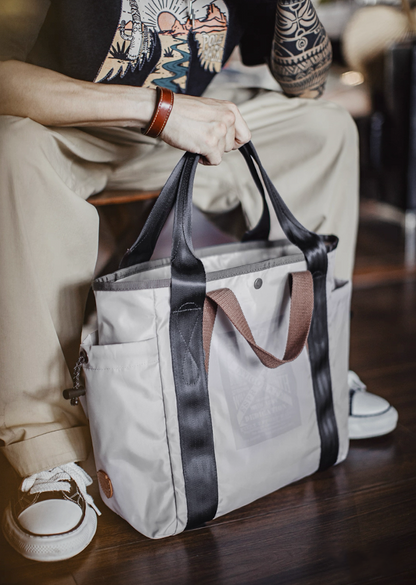 Model seated holding Ash Gray water-resistant tote bag with black straps