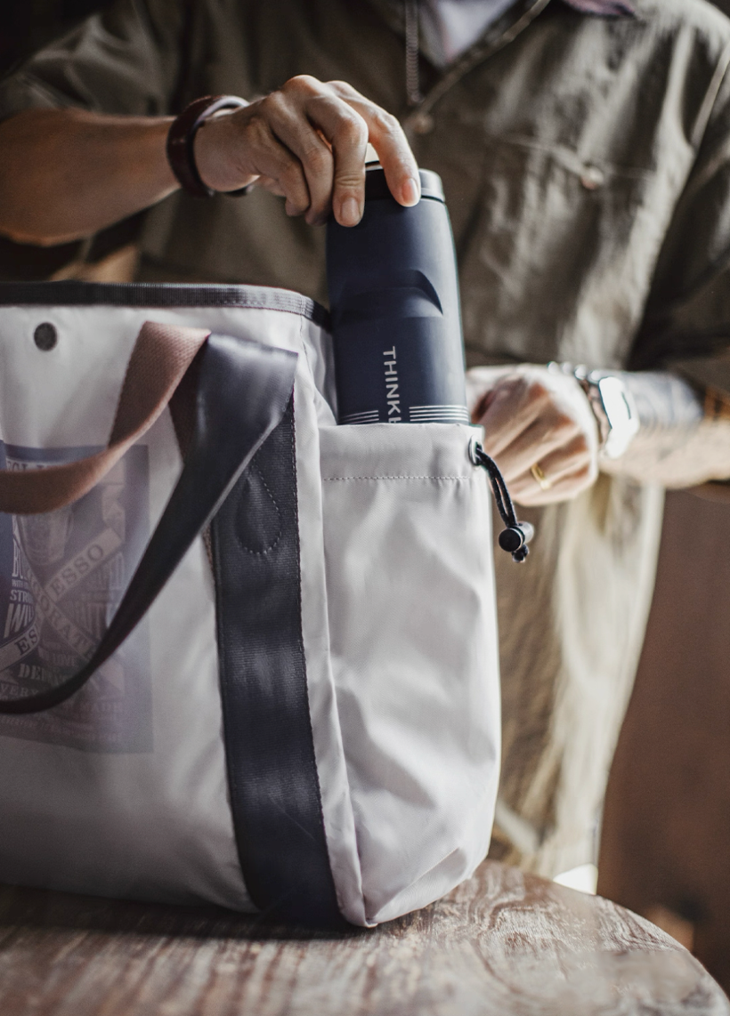 Side drawstring pocket of outdoor tote bag holding reusable bottle