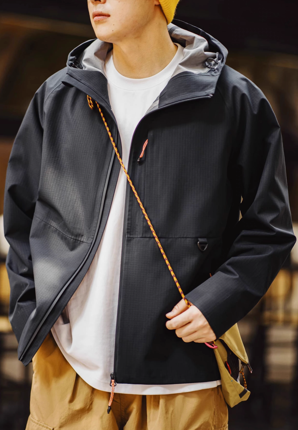 Black ripstop shell coat with adjustable hood worn casually showing lightweight design and streetwear styling