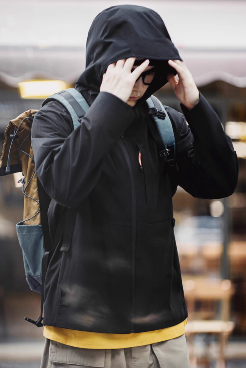 Black waterproof ripstop shell coat with hood styled for outdoor travel paired with backpack and casual layering