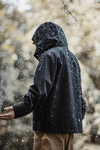 Black all-weather ripstop shell coat demonstrating waterproof performance with water droplets repelling off fabric