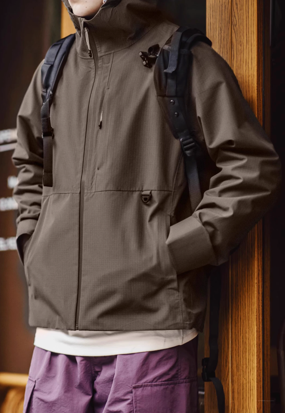 Khaki waterproof ripstop shell coat styled with backpack for outdoor commuting featuring clean silhouette and functional pockets